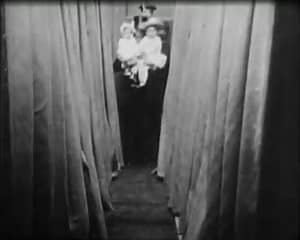 A film still from A Trip to Salt Lake City. A polygamist husband in a top hat uncomfortably carries three small children into a Pullman sleeping car.