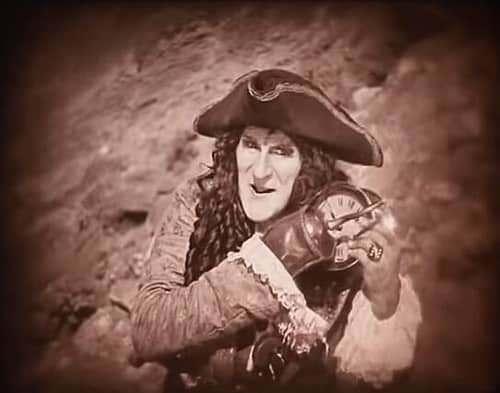 Ernest Torrence as Captain Hook holds a clock to feed to a hungry crocodile.